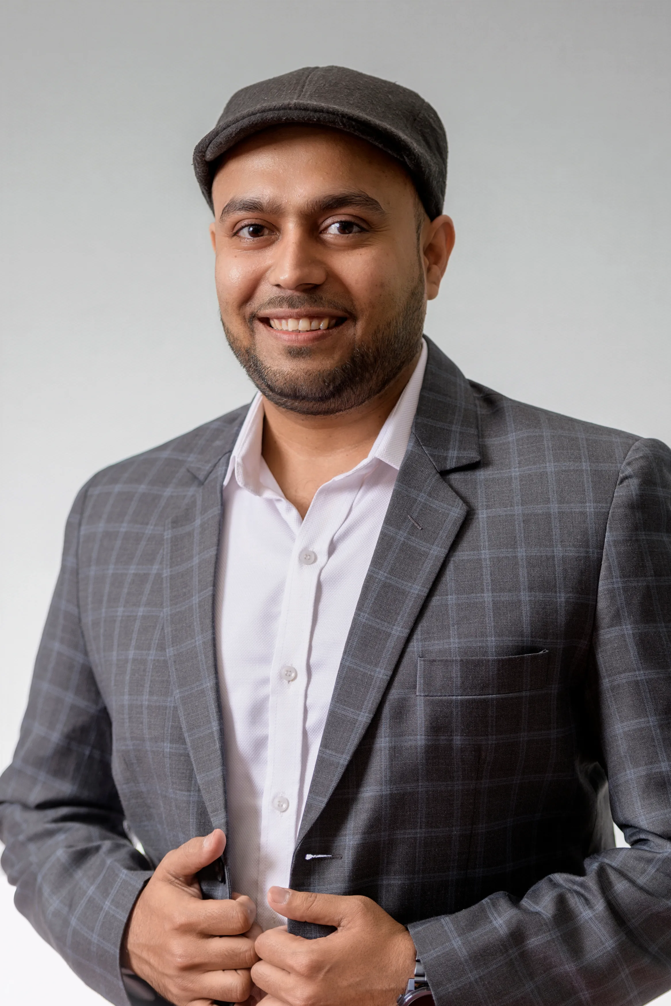 Professional headshot of a man in a flat cap and check blazer