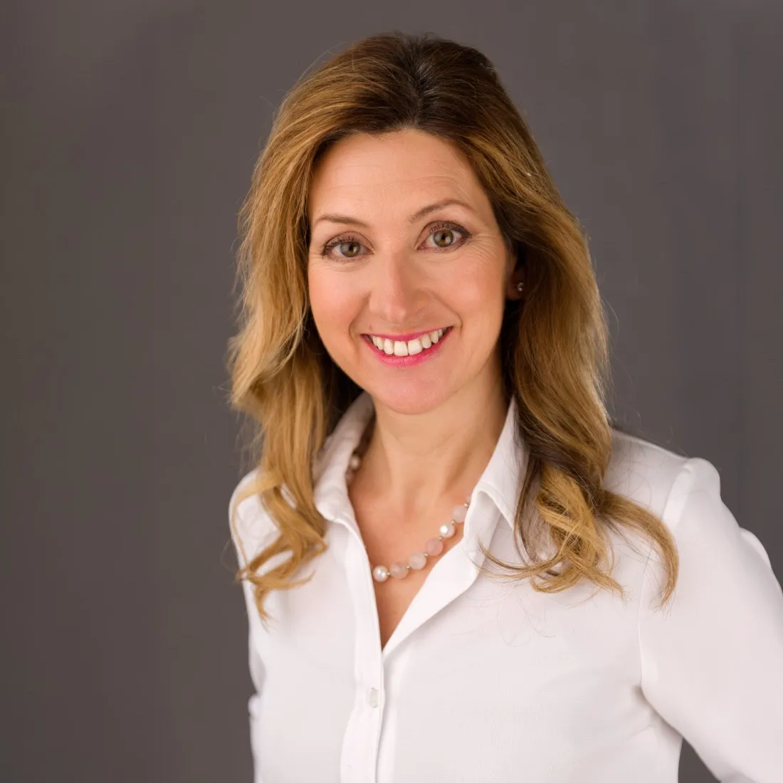A smiling woman with long fair hair in a white shirt