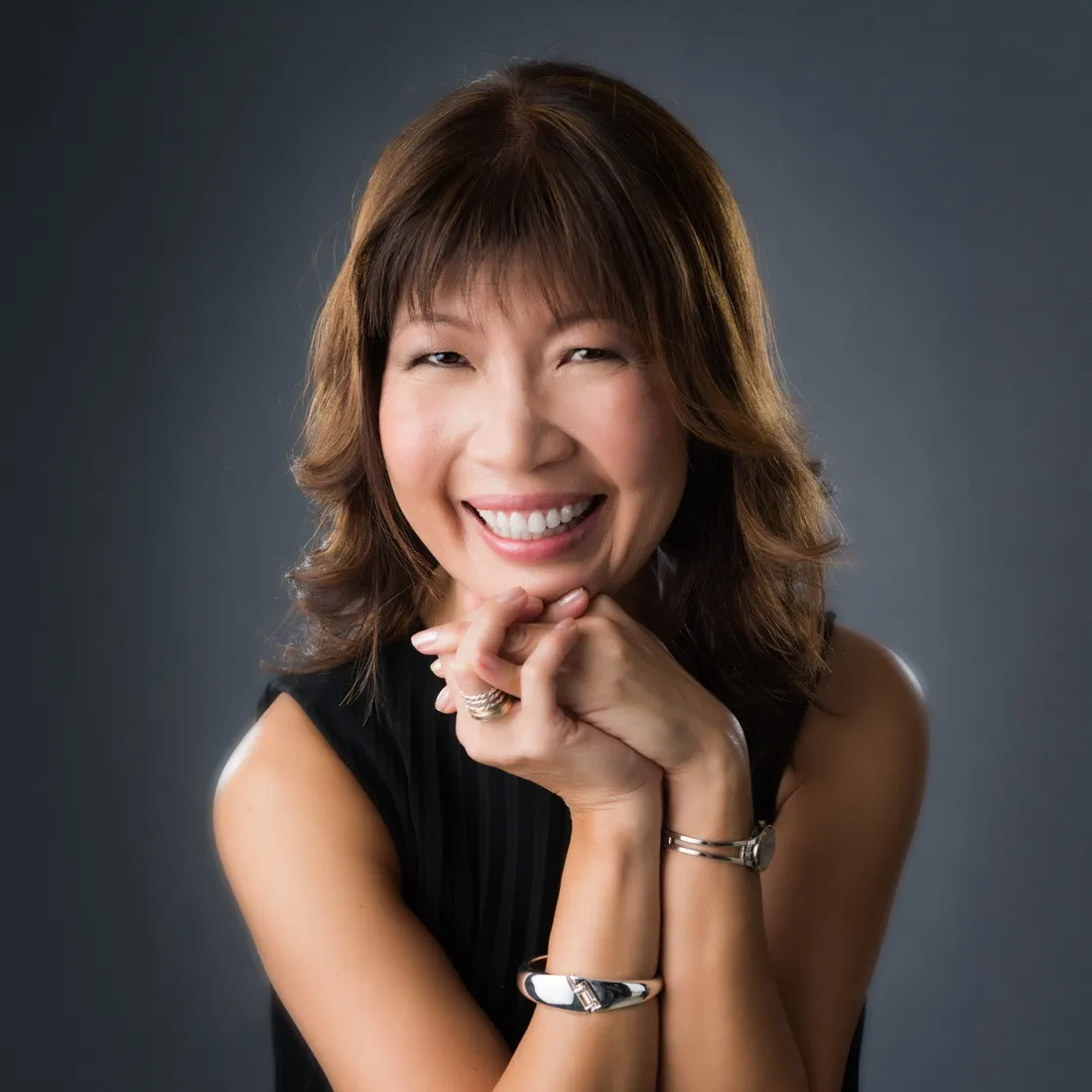 A laughing woman in a black top resting her chin on her folded hands