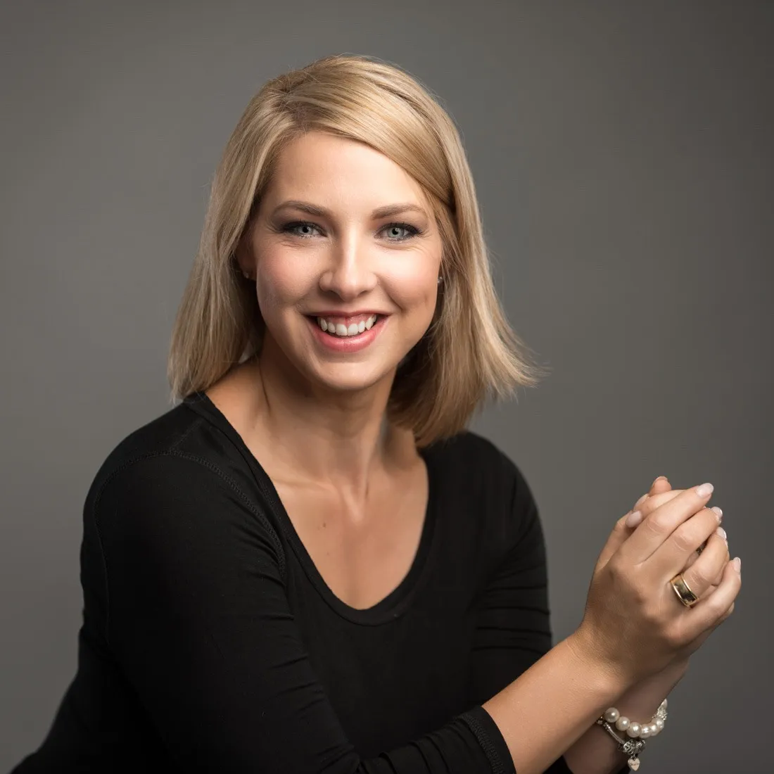 A smiling woman in a black top with her hands clasped