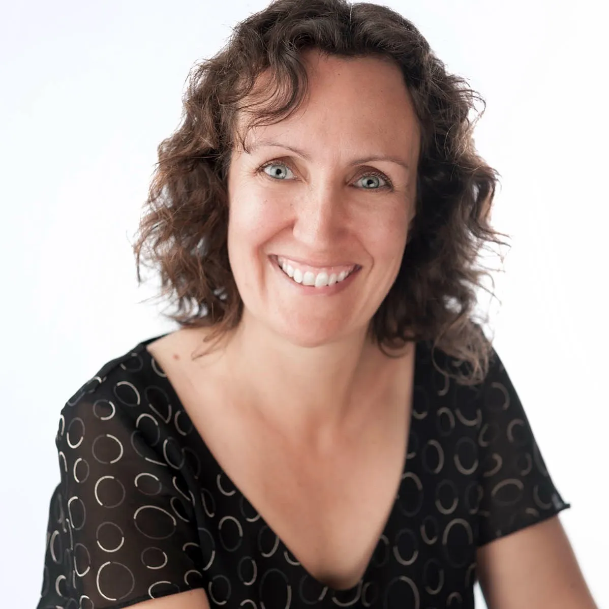 A smiling woman with curly hair in a black patterned top against a white background