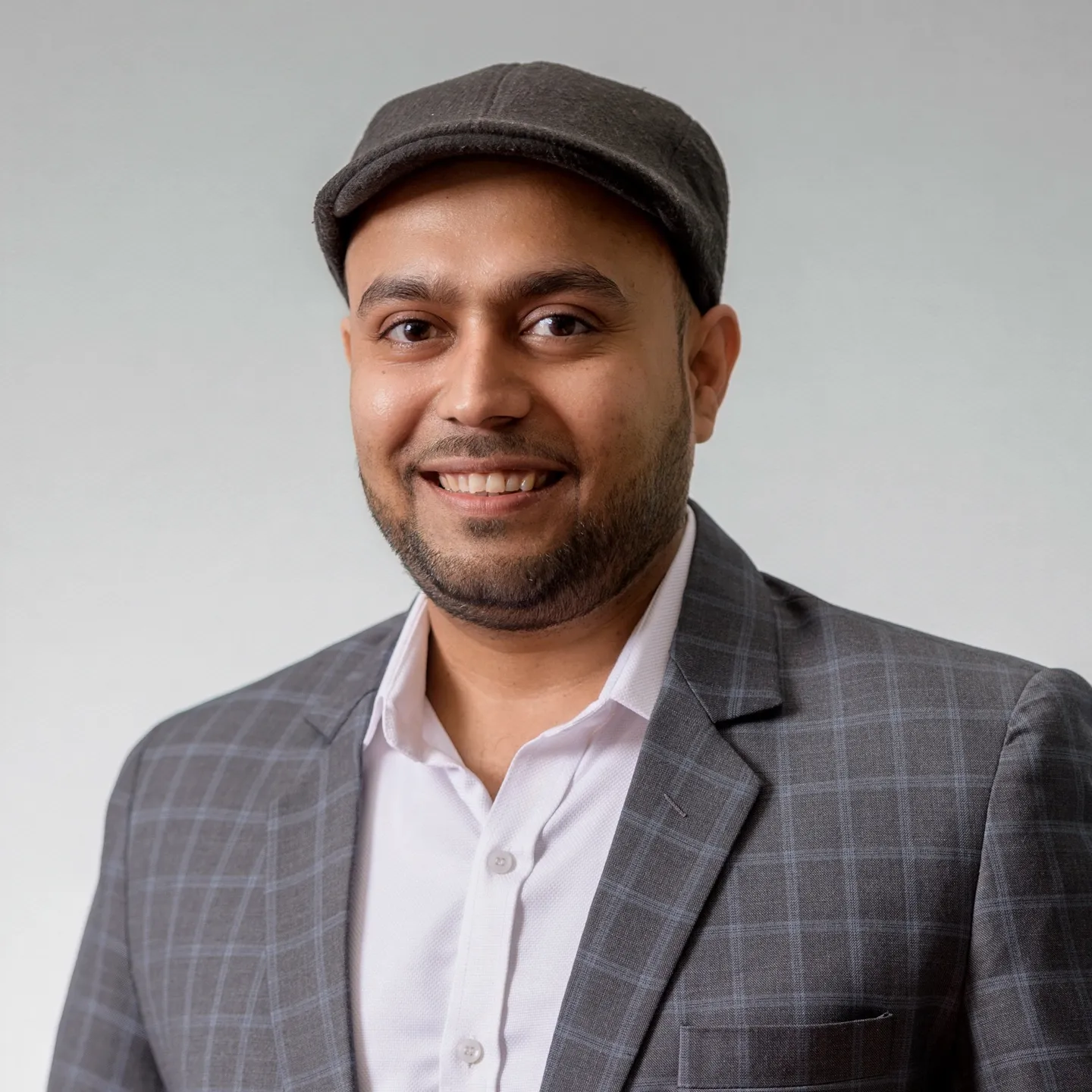 A smiling man in a cap and checked blazer