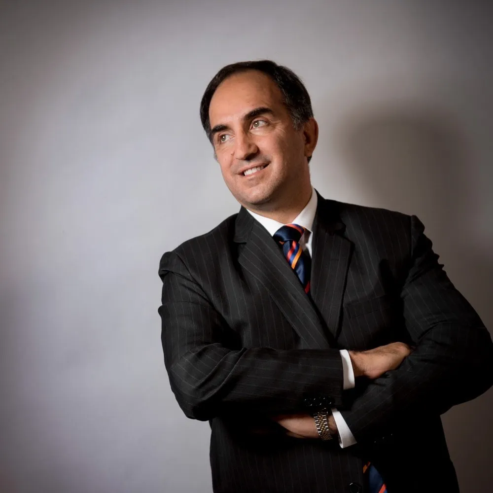 A man in a dark suit and striped tie standing with his arms folded