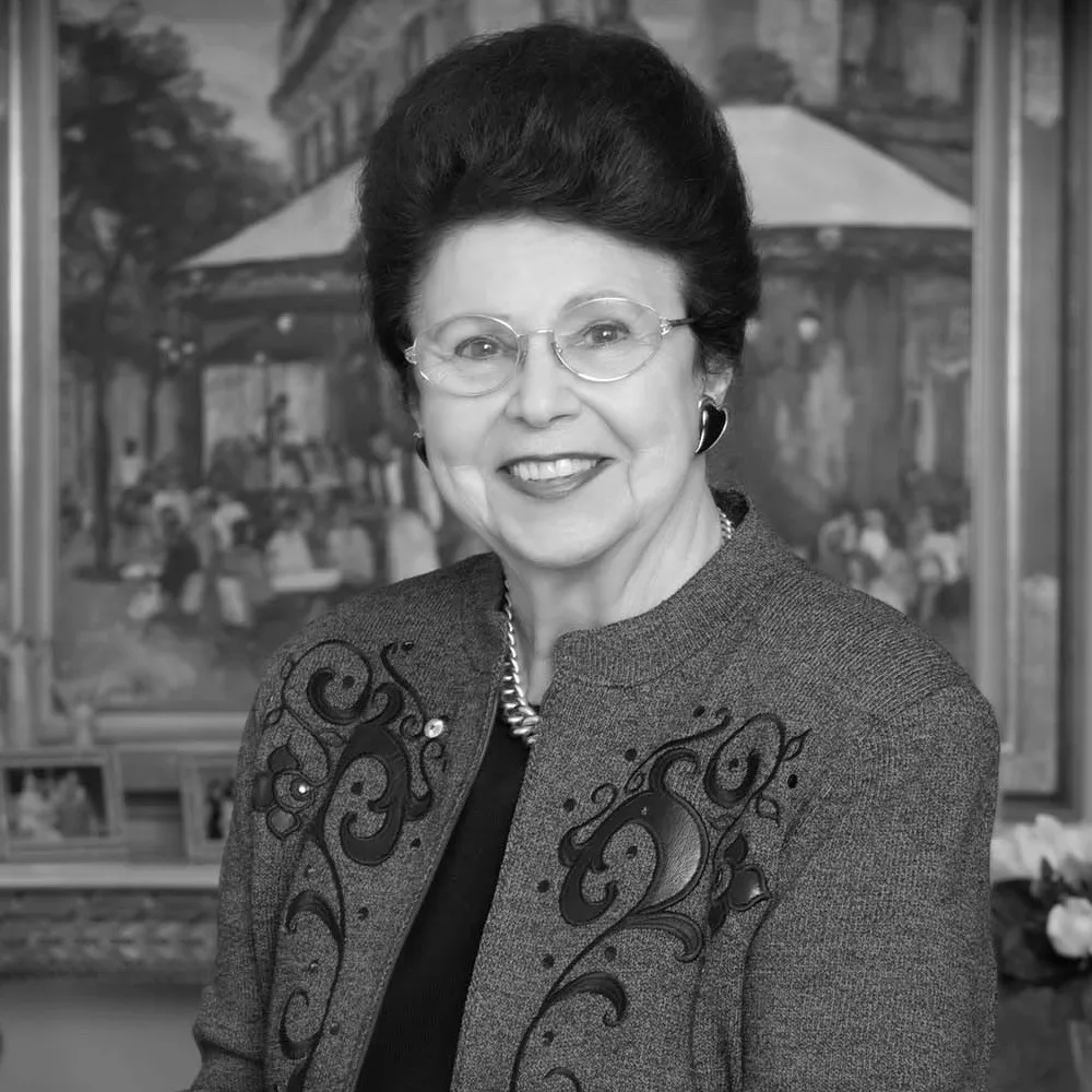 A smiling woman in glasses and an embroidered jacket, in black and white