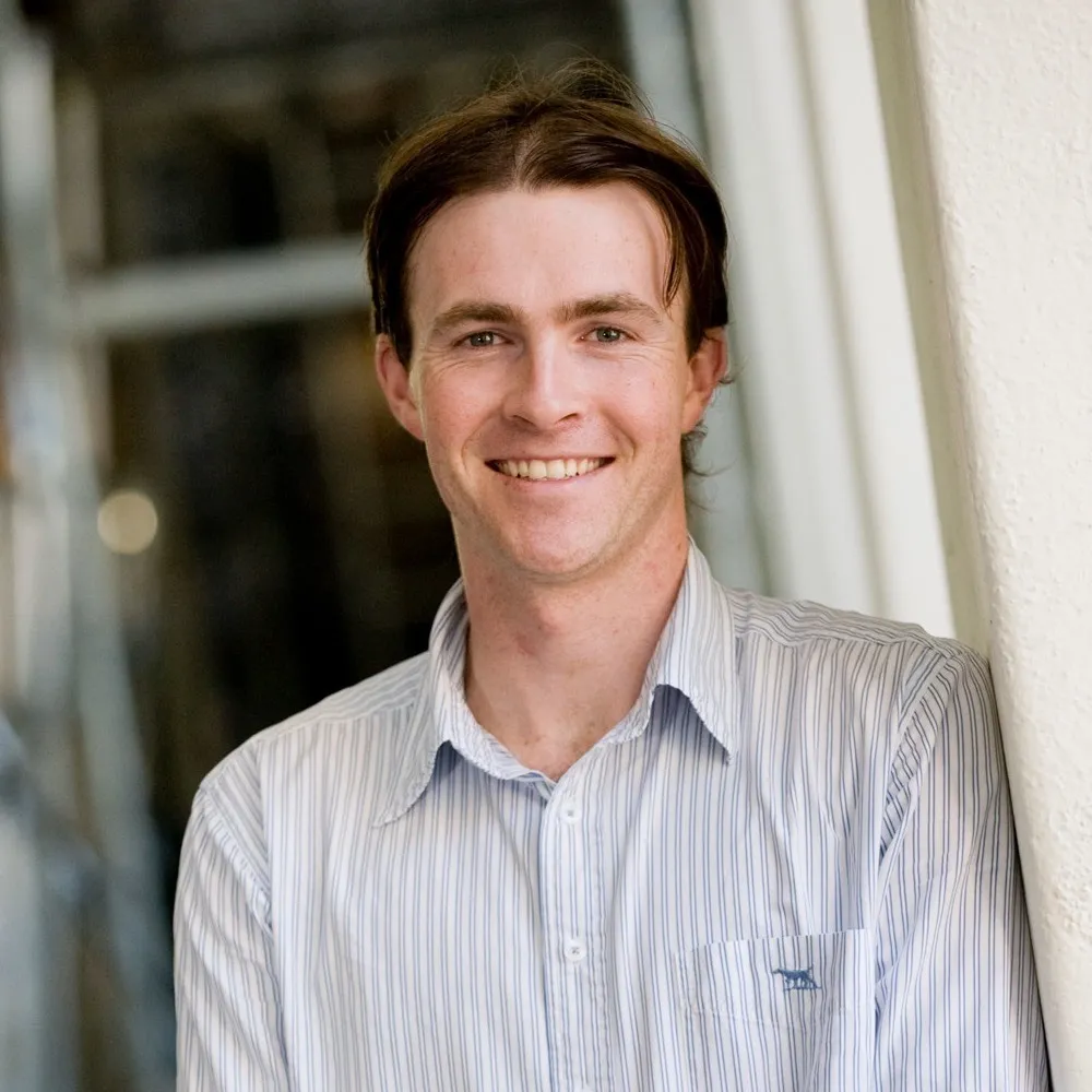 A smiling young man in a striped shirt beside a window