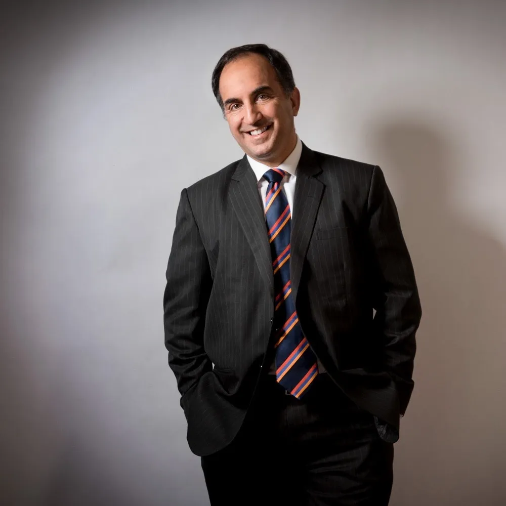 A man in a dark suit and striped tie with one hand in his pocket