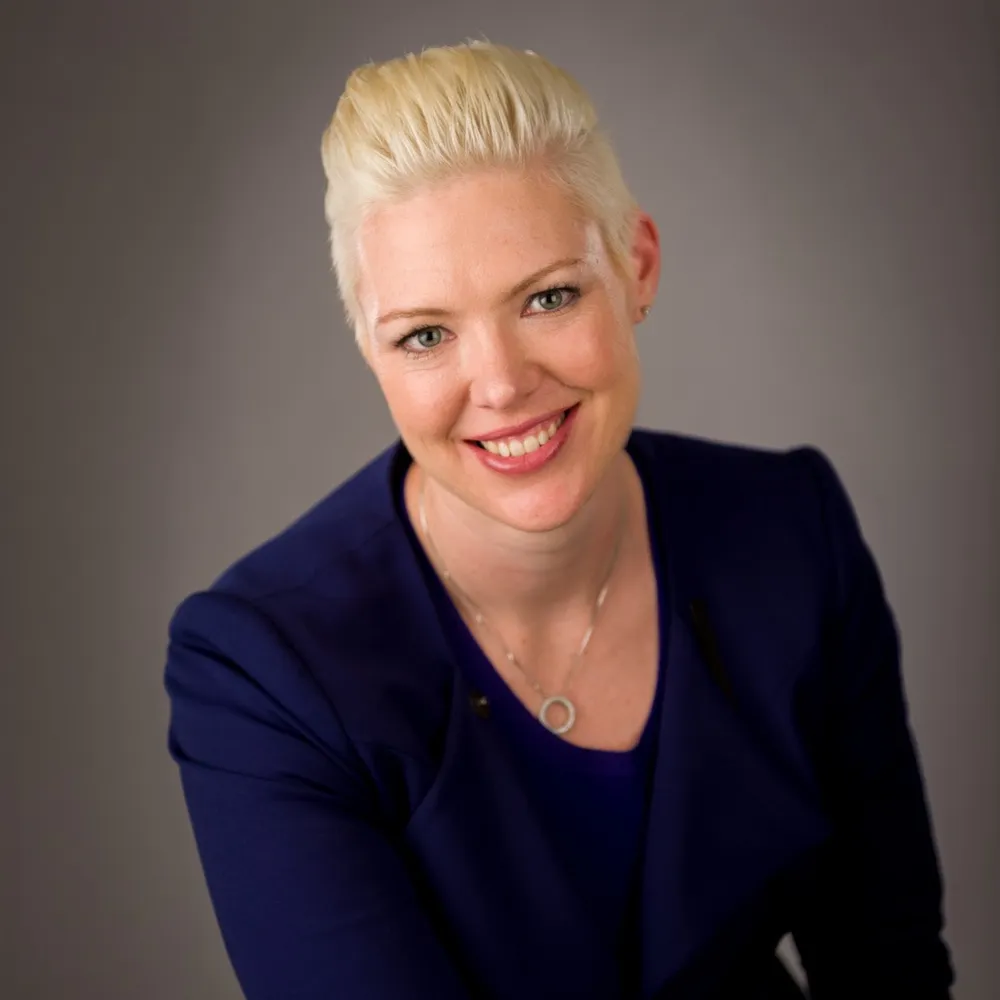 A smiling woman with short blonde hair in a navy blazer