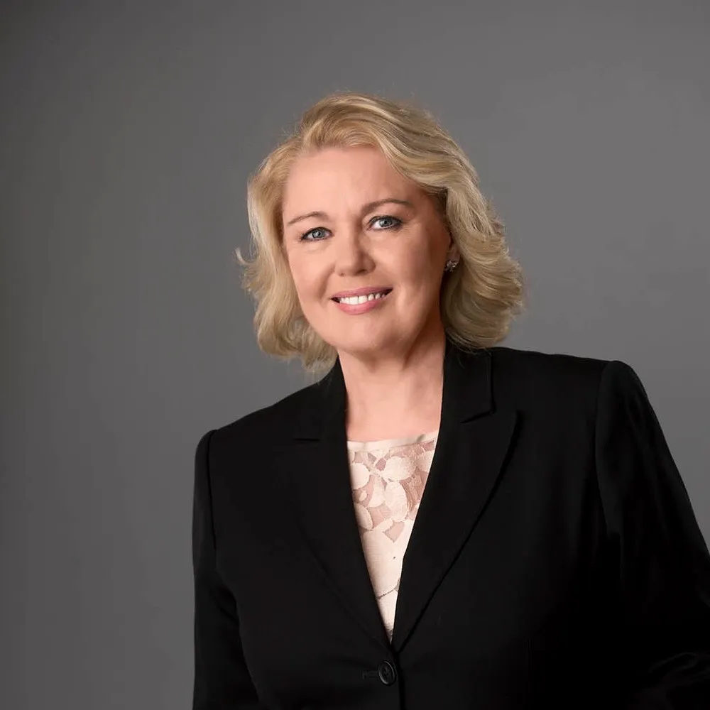 A smiling woman with short fair hair in a black jacket