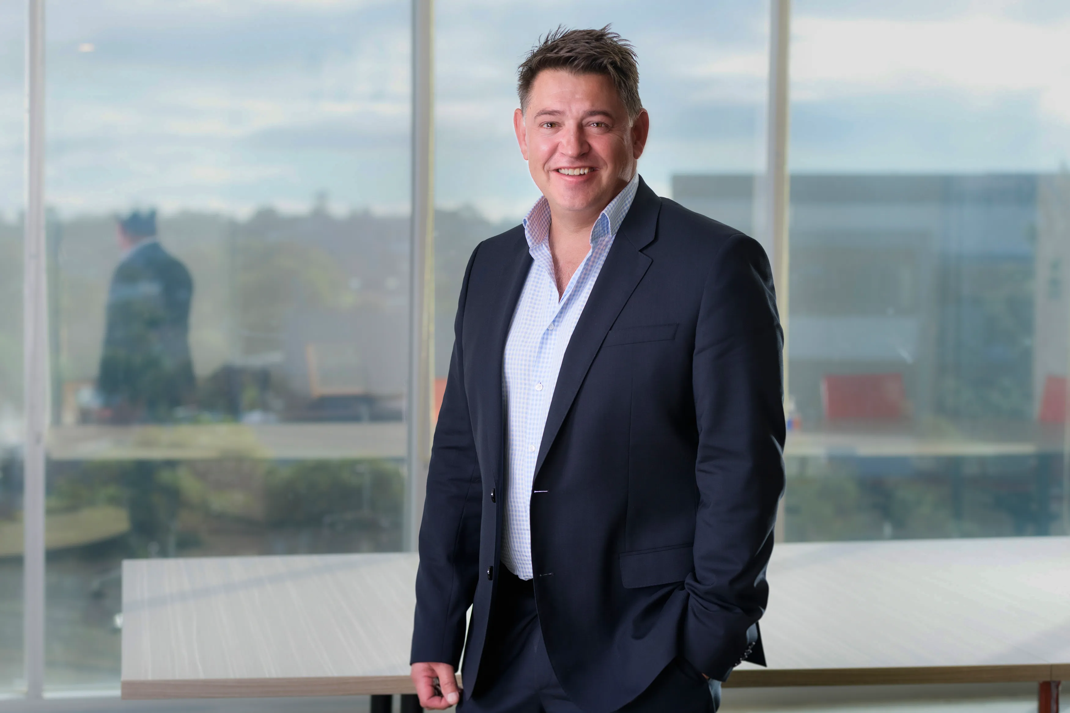 Executive headshot of a man in a navy suit against office glass