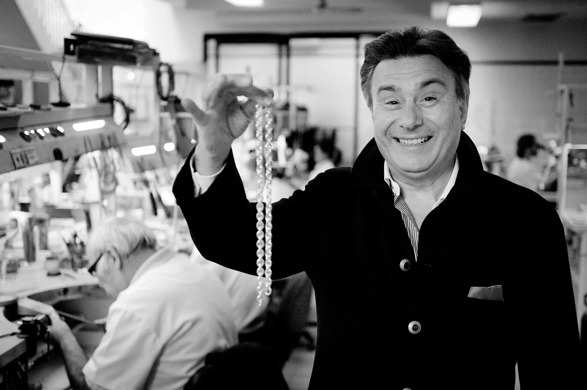 A jeweller photographed holding a strand of pearls in his workshop