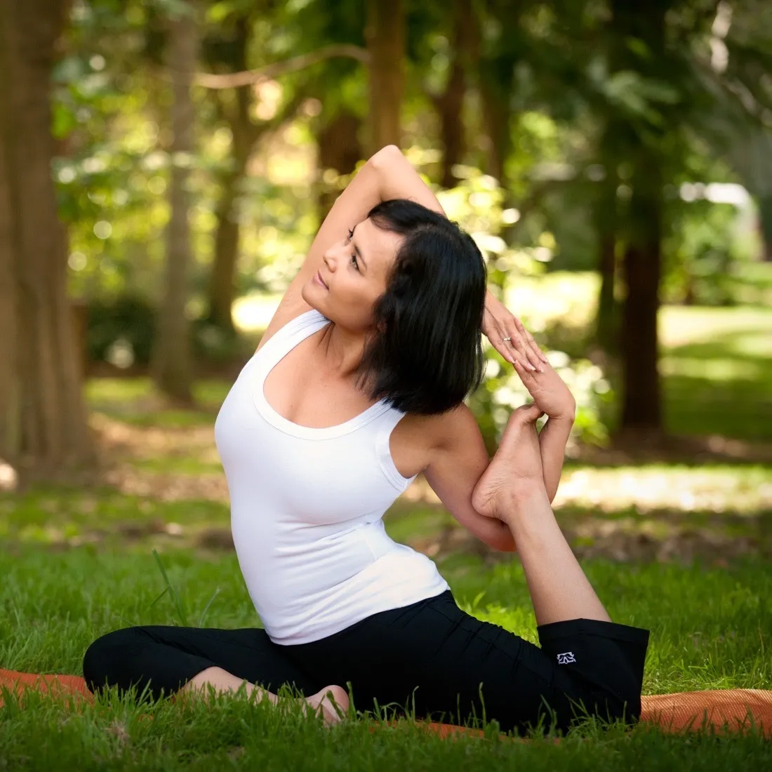 A woman holding a yoga pose on the grass among trees