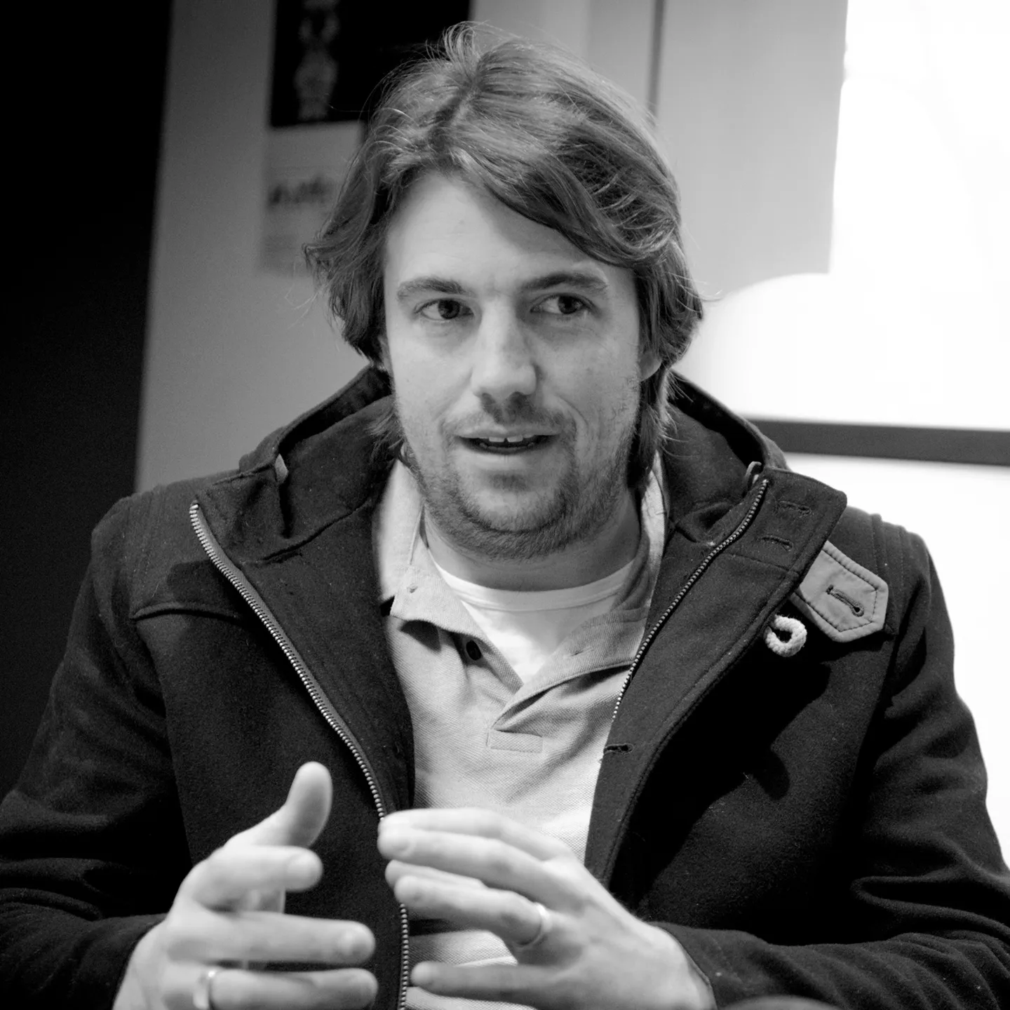 A man in a dark jacket talking with his hands, in black and white