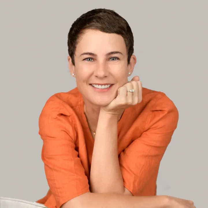 A smiling woman in an orange shirt, her chin resting on one hand: the frame chosen as her photograph