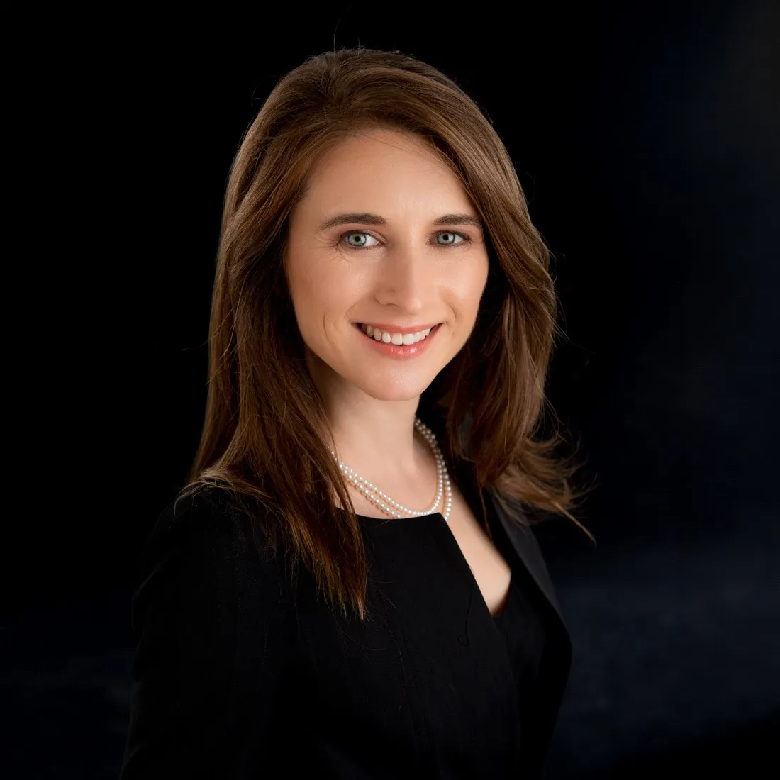 A smiling woman with long brown hair in a black top against a dark background