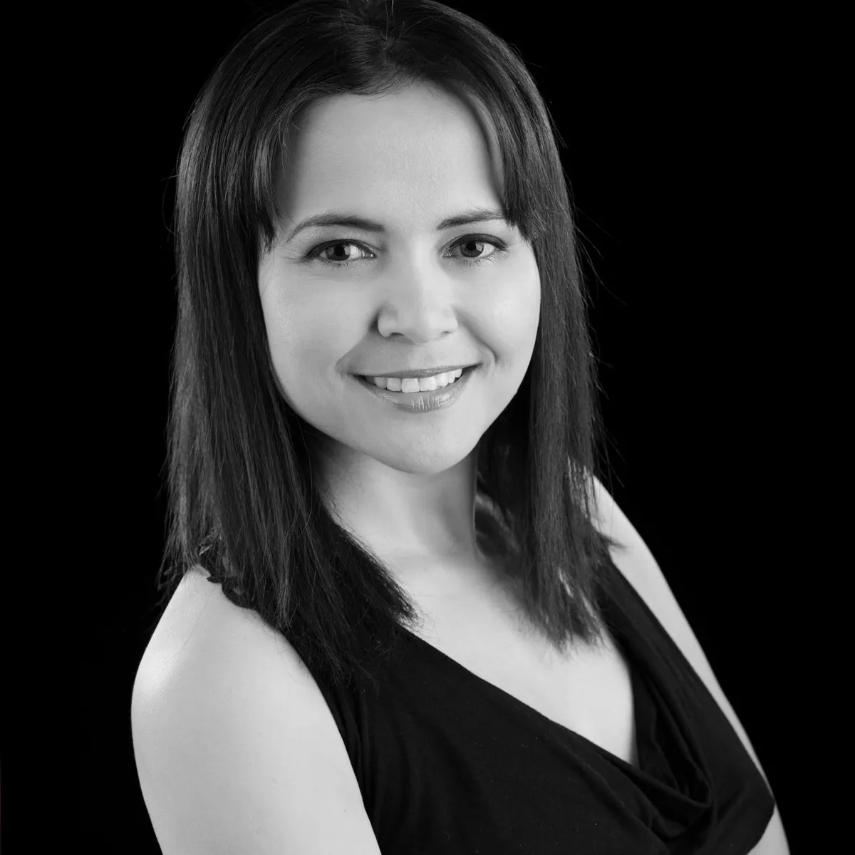 A smiling woman with long dark hair in a black top, in black and white