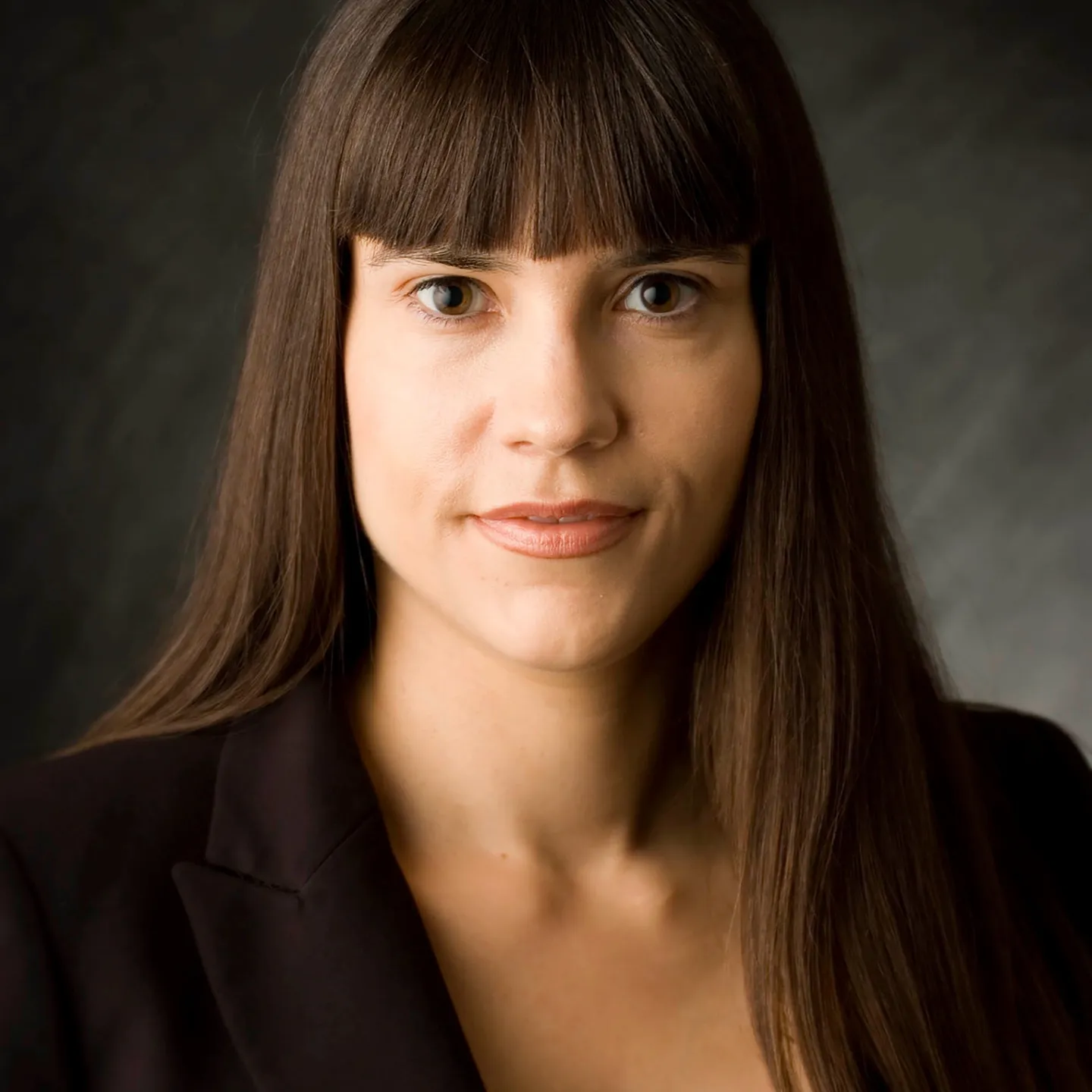 A woman with long dark hair and a fringe in a dark jacket