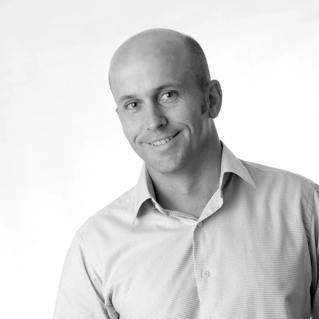 A smiling man in an open-collared shirt, in black and white