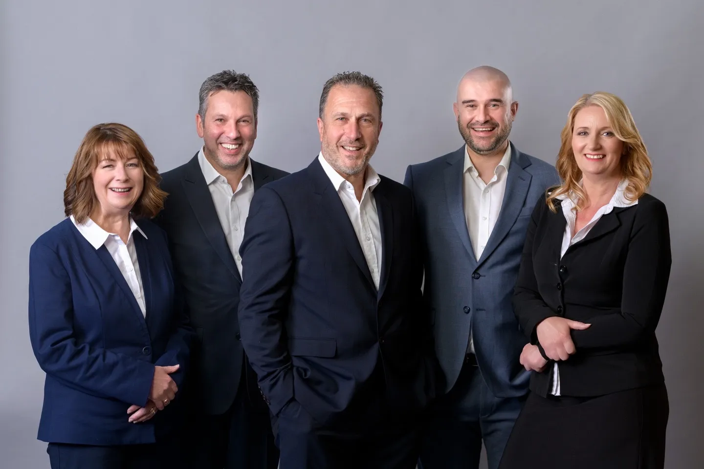 Five colleagues in business suits photographed together against a grey background
