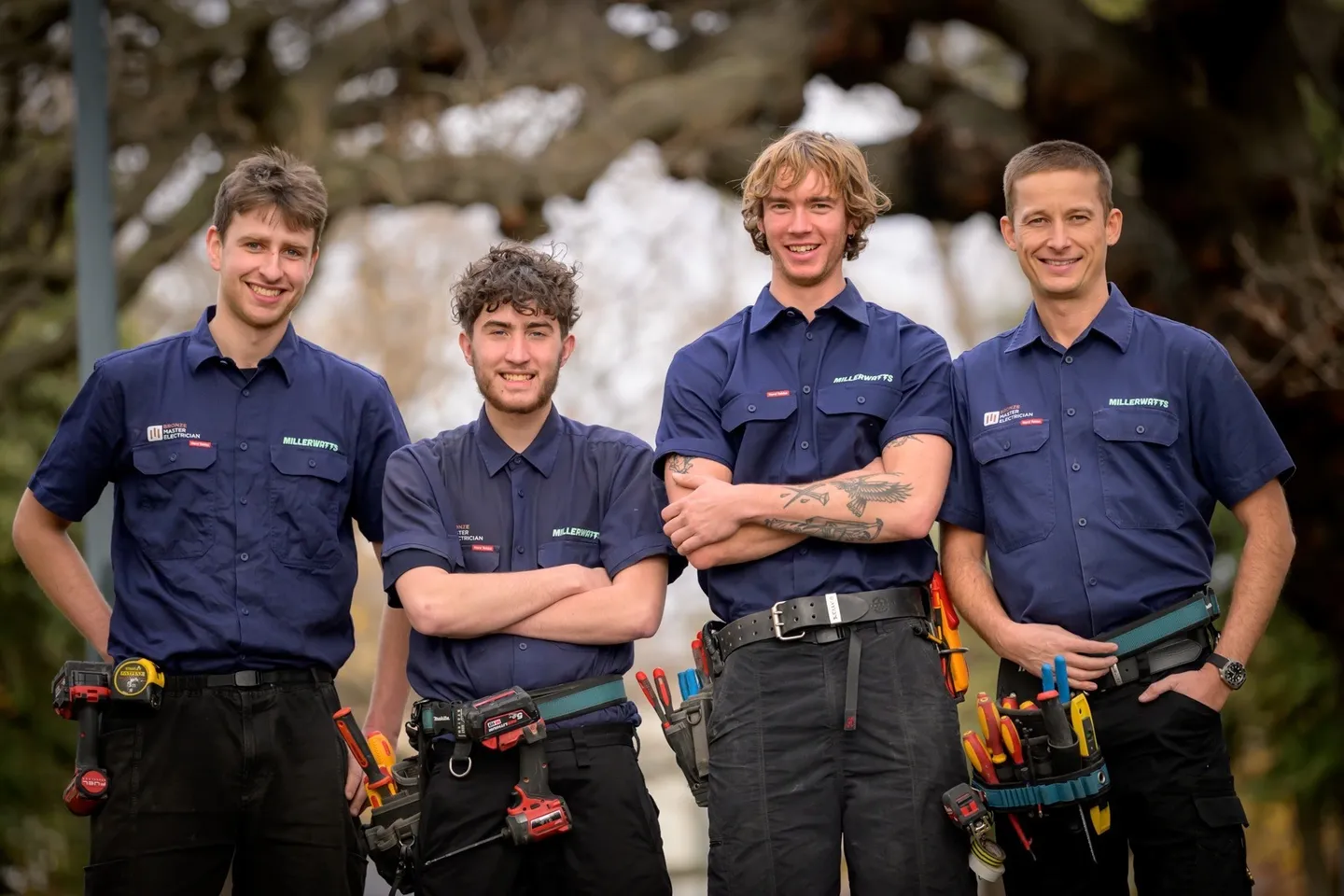 Four tradespeople in matching navy work shirts and tool belts