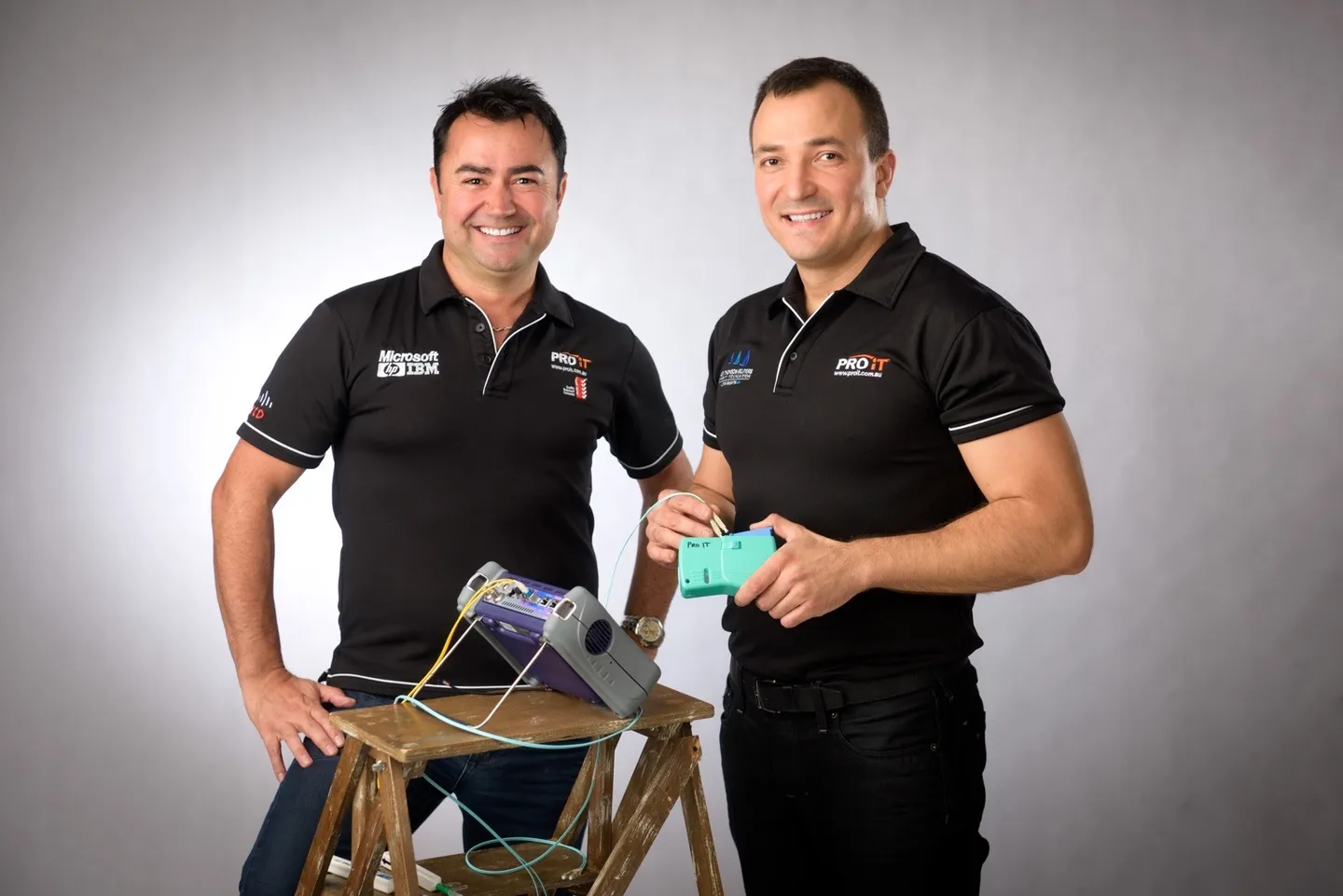 Two men in matching black work shirts with the tools of their trade